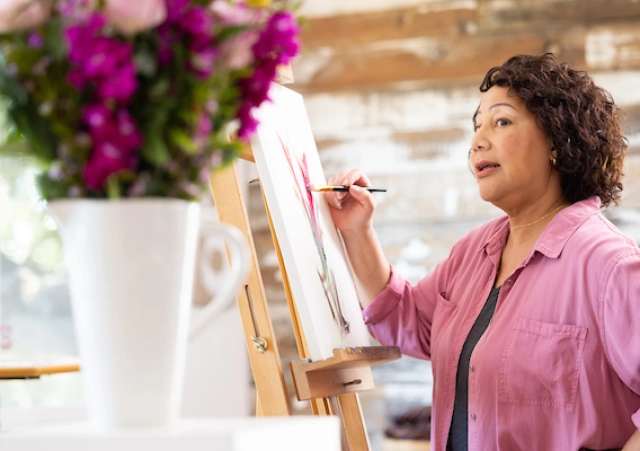 woman in pink shirt painting a vase of flowers